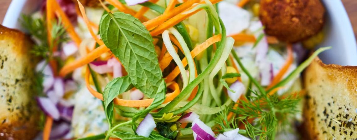 Vibrant salad featuring fresh vegetables, falafel, and herbs in a white bowl, perfect for a healthy meal.